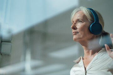Smiling senior woman listening music through wireless headphones