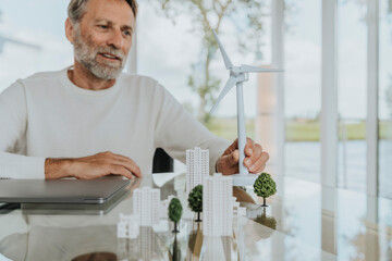 Smiling mature man with wind turbine model sitting at table