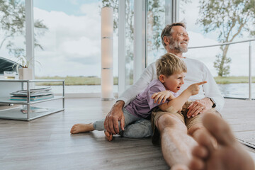 Happy father with son pointing finger sitting on floor at home