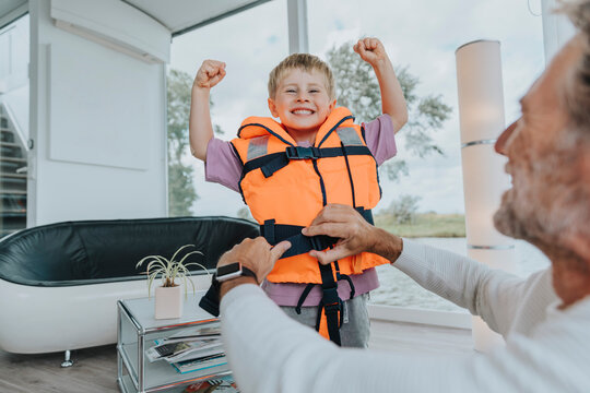 Happy son wearing life jacket flexing muscles at home
