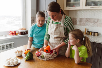 Girls looking at mother taking vegetables from mesh bag in kitchen