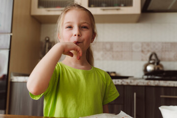 Smiling girl licking finger in kitchen at home