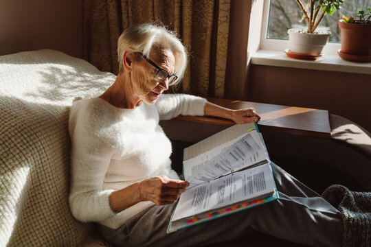 Woman wearing eyeglasses reading documents sitting in living room at home