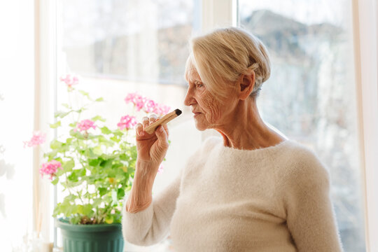 Senior woman smelling palo santo stick at home