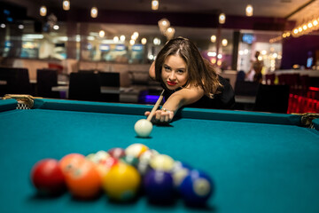 Young happy girl holding cue and play billiard at pub