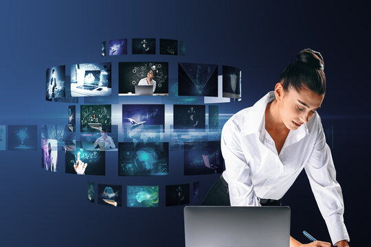  businesswoman leaning and writing something on desktop with laptop and creative digital picture gallery on blue background. Photo album and media technology concept. Going through images.