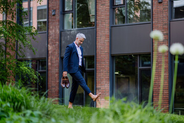Businessman walking barefoot in park, feeling free, work life balance concept.