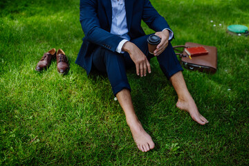 Businessman having coffee, resting and sitting barefoot in park, feeling free, escaping from work,...
