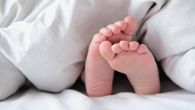 child sticks legs out from under the white blanket in the morning. kid wake up in a cozy bed and waves his leg