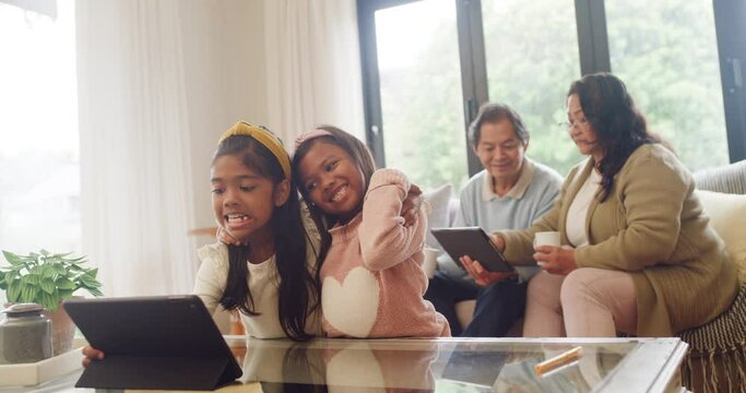 Girls playing with a digital tablet in the living room with their grandparents babysitting. Happy silly sisters pulling faces and taking selfies with grandmother and grandfather talking on the sofa