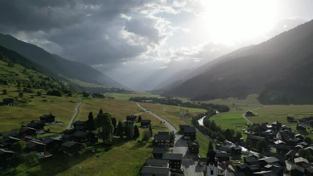 Drone footage of cloudy morning in Alpine valley with small village on foreground and mountains on background 