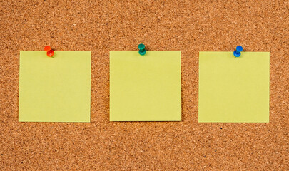 Three Yellow Post-it Sticky Notes on a cork board with drawing pins. Copy space