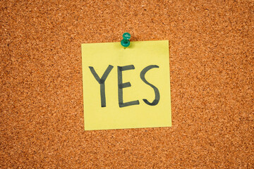 Yellow Post-it Sticky Note on a cork board with drawing pin. Yes
