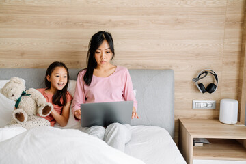 Asian mother and daughter using laptop while sitting on bed
