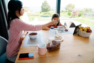 Asian girl using tablet computer while having breakfast with her mother