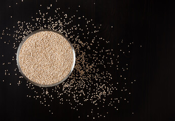 Dried white quinoa seeds in glass bowl on black wooden background