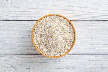 Dry sesame seeds in wooden bowl on white wooden background