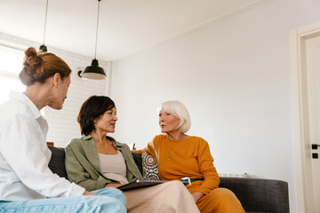 Mature three women talking and smiling while sitting on sofa