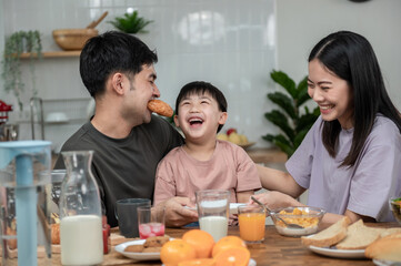 Happy Asian family enjoying breakfast together on dinning table. Young Asian father eating bread with family his son and wife having breakfast in the kitchen. Happy Asian family lifestyle concept.
