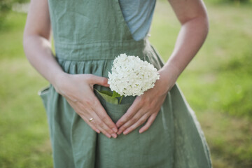 gardening and profession concept - young woman in apron holding flowers in the garden in summer
