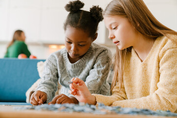 Naklejka premium Adopted sisters solving puzzles sitting on couch