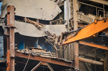 Hydraulic scissors on rigging demolish industrial building