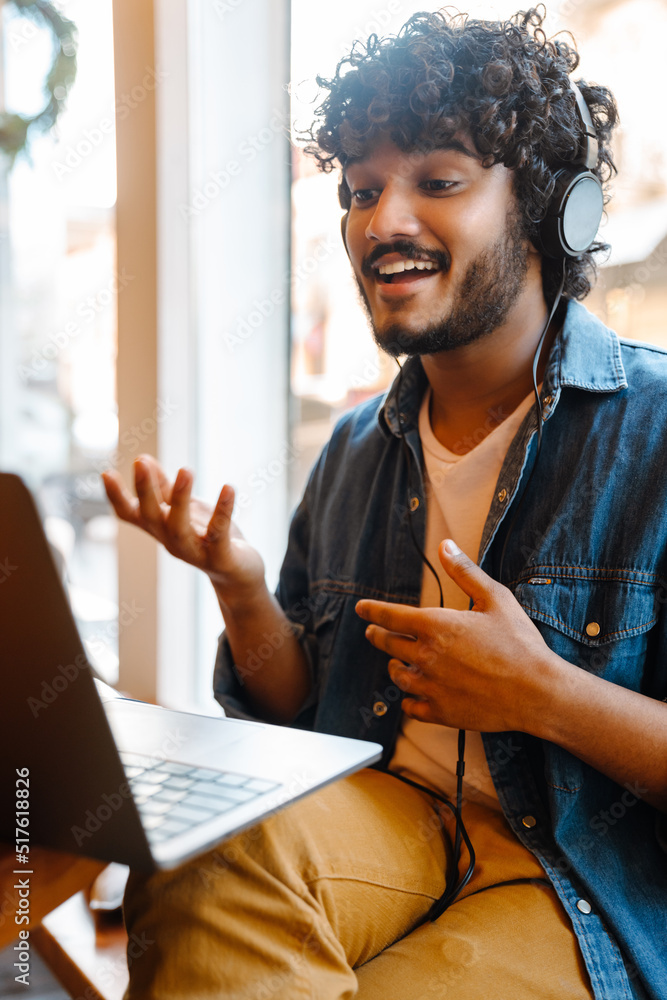 Wall mural Young smiling handsome indian curly man holding videoconference with laptop