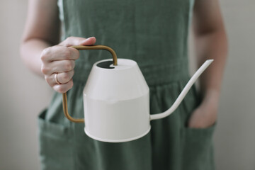 Girl in apron holds a watering can. Watering and caring for home plants. home gardening. hobby flower cultivation