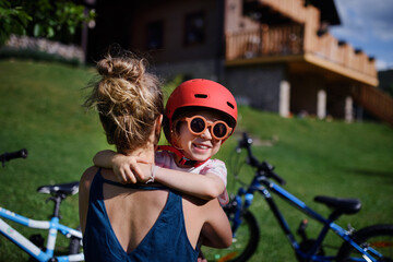 Fototapeta premium Young mother with little daughter preaparing for bike ride, putting on helmets and hugging.