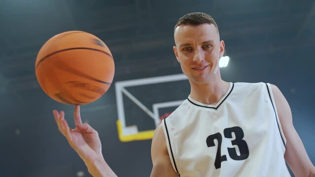 Sport lifestyle, young man basketball player shows a trick with a spinning ball on his finger, looking at the camera, 4k slow motion.
