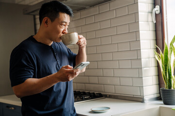 Adult calm asian man with phone and cup of tea