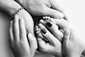The palms of the parents, the eldest child holds the feet of the newborn child. The newborn's legs are in the hands of the mother's father and older brother and sister. Macro photo of foot, heels toes