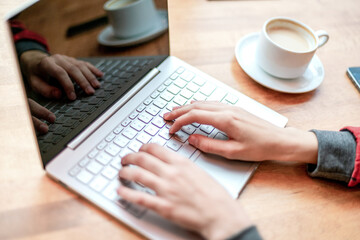 Fototapeta na wymiar Hands typing on keyboard of laptop at coffee desk.