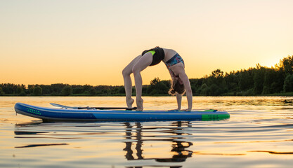 Sport woman yogini scorpion pose practice yoga exercise on sup board on the sea in relaxing day ,...