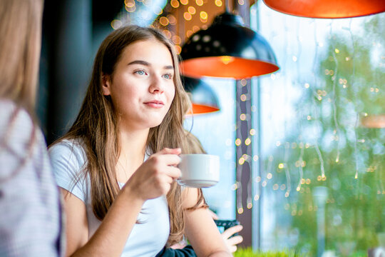 A girl is holding a cup of coffee sitting in cafe.