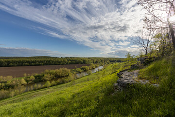 Obraz premium View of the countryside. bright greenery in the ravine. Saturated green grass against the blue sky. Plowed field on the horizon.