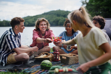 Group of multiracial young friends camping near lake and and having barbecue together, looking at...