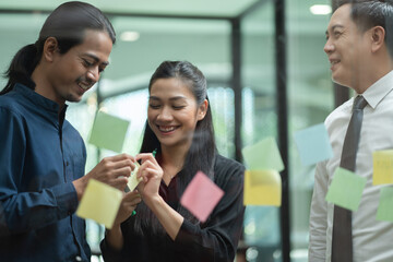 Asian business team meeting in the office using post it notes stick on glass wall. Corporate people brainstorming idea for project together.