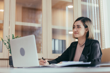 Businesswoman entrepreneur or manager working on paperwork and using laptop for internet searching at desk in the office.