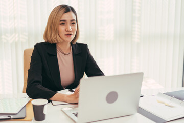 Young Asian businesswoman or manager video meeting with customer on laptop in the office. online conference or interview for job applicant