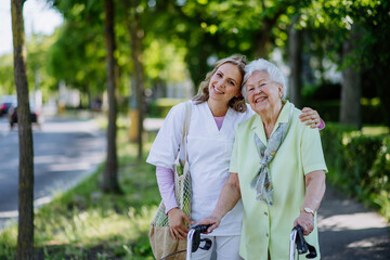 Portrait of caregiver with senior woman on walk in park with shopping bag, looking at caemra.