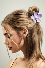 Cropped close-up shot of a blonde girl with a claw clip in her hair. Portrait of a young woman with a violet flower hair claw clip on a pastel background. Side view.