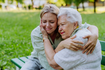 Worried senior grandmother comforting grown up granddaughter when sitting on bench in park, share...