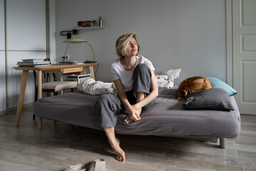 Loneliness at midlife. Thoughtful sad middle-aged Scandinavian woman sitting on sofa with dog...