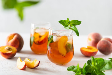 Fresh Peach iced tea. Iced tea with peach slices, mint and ice cubes on a white background. Close up. Homemade refreshing summer drink recipe. Refreshing peach lemonade. Summer cold drink