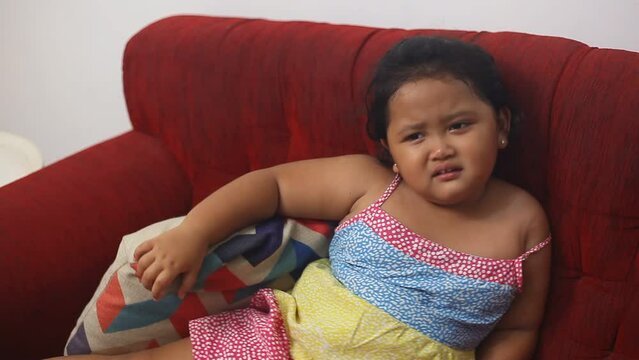 Cute asian little girl sulking while siiting on the sofa at home