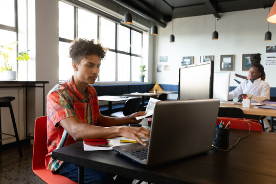 Biracial young businessman using laptop at desk in creative office