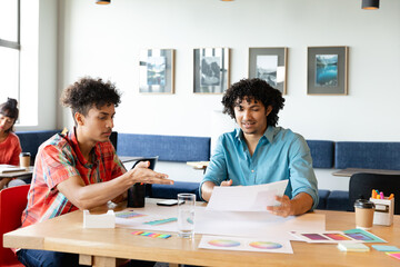Fototapeta premium Creative biracial businessmen discussing over charts at table in office