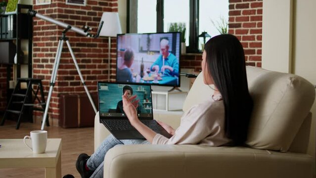 Asian woman discussing with coworker on internet conference while doing remote work. Office employee working remotely while attending online video call with executive manager on laptop at home