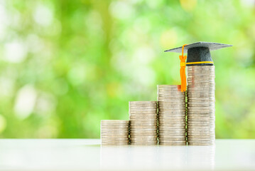 Graduate study abroad, education concept : Graduation cap sits atop stacks of coins, depicting...